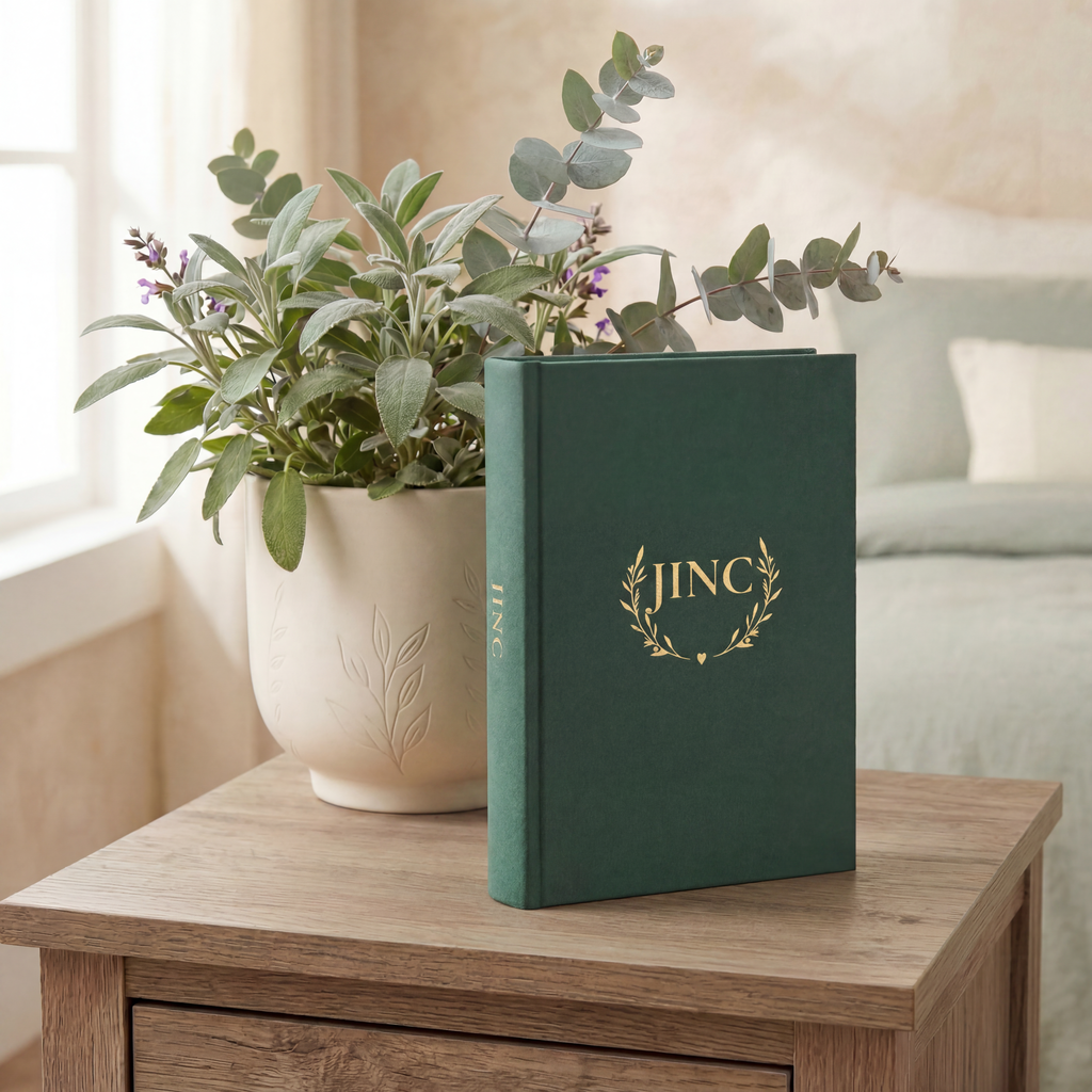 Green book with 'JINC' logo on a wooden surface next to a potted plant